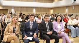 Zdjęcie przedstawia cztery osoby siedzące na Auli podczas Forum Pomocy Społecznej na tle tłumu uczestników