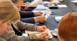 Osoby siedzące przy stole analizują papiery i prowadzą dyskusję.