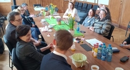 Osoby zgromadzone przy stole, uczestniczące w dyskusji w przyjaznej atmosferze.