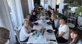 Przy stole siedzi kilka kobiet, które jedzą i rozmawiają, tworząc przyjemną atmosferę