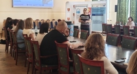 Grupa ludzi siedzi przy stole w pomieszczeniu, prowadząc rozmowę i d