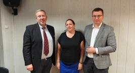 Trzy osoby stoją przy ścianie w sali posiedzeń; ujęcie pamiątkowe po spotkaniu